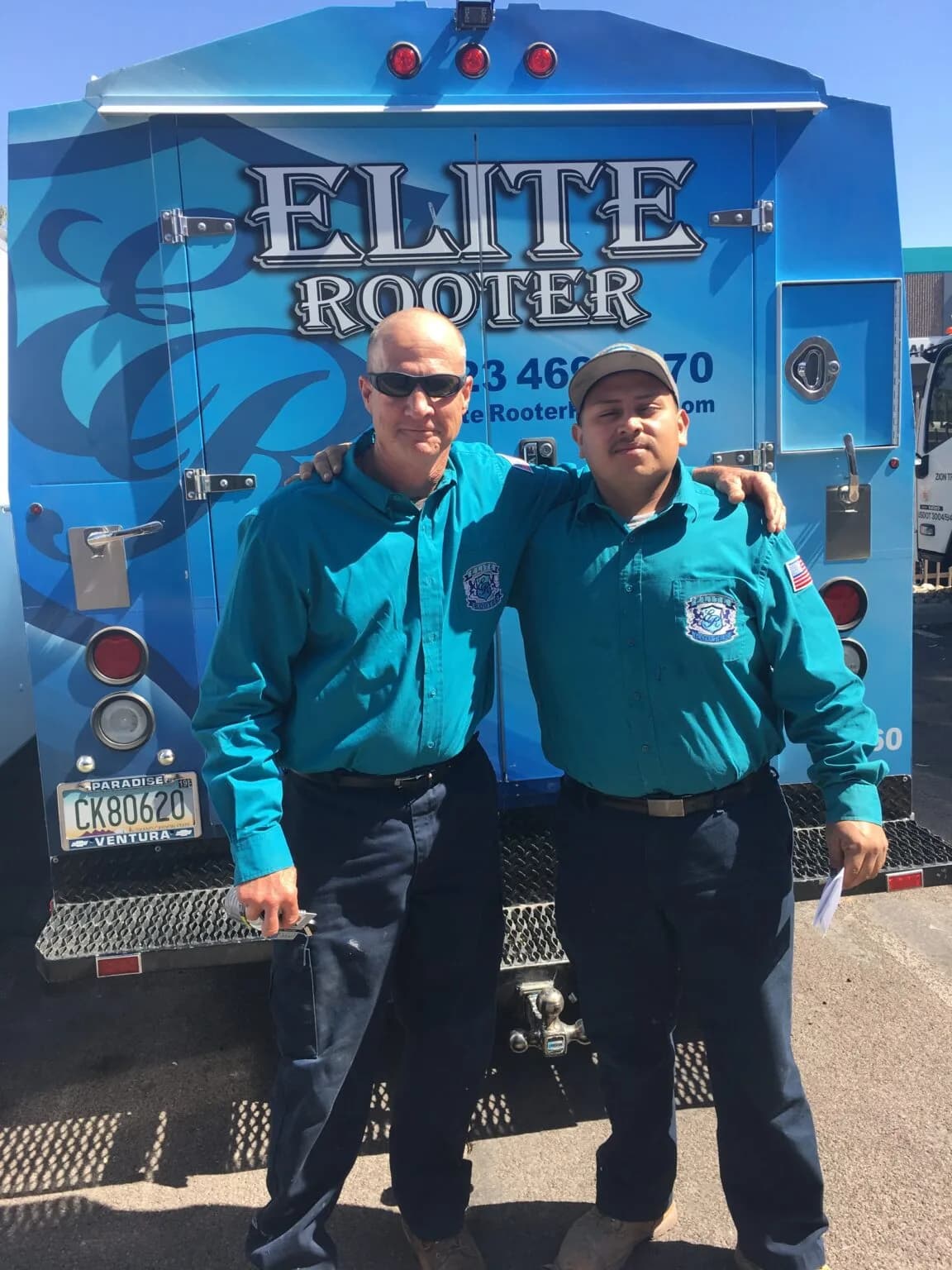 Two Elite Rooter technicians standing in front of a company service truck