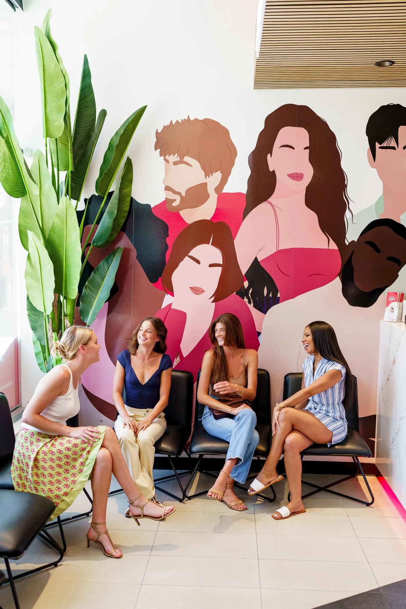 Guests waiting in a Hello Sugar salon lobby in front of the brand's portrait mural